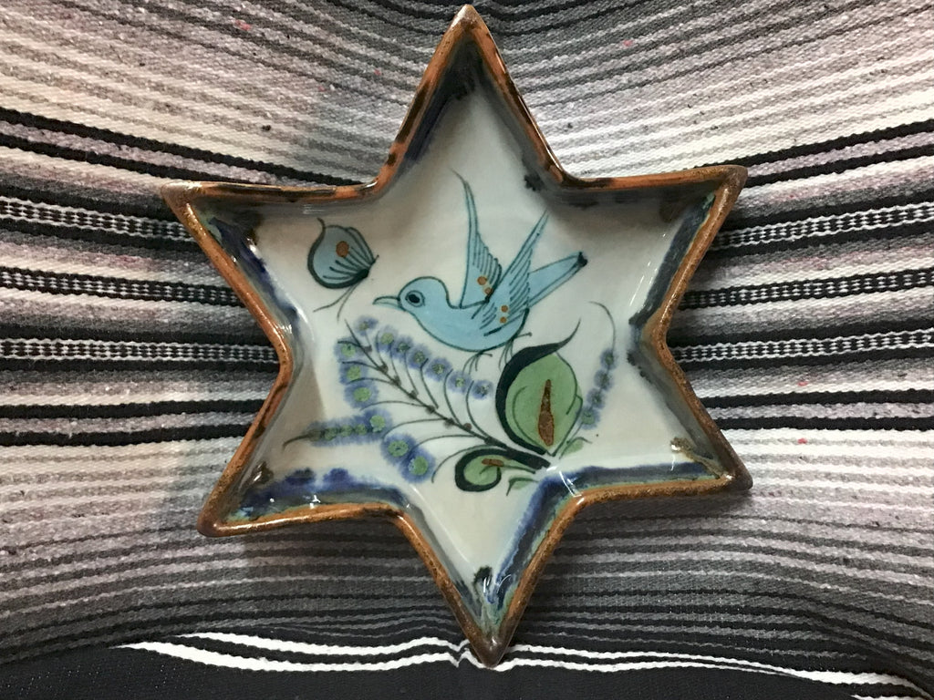 Star-shaped ceramic dish with bird design on a striped fabric background