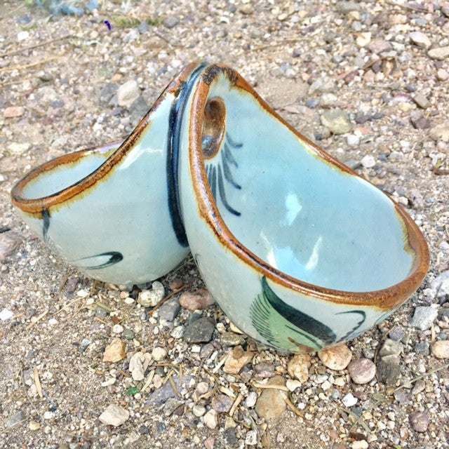 Ken Edwards Stoneware Pottery in natural grey clay color with brown rim and blue, green, and black birds, butterflies and leaves decorated on the exterior on vases, interior on plates , trays and triviets. this is a double dipper salsa bowl or a hanging double plant holder.