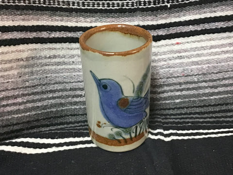 Cylindrical ceramic vase with a blue bird design on a striped fabric background