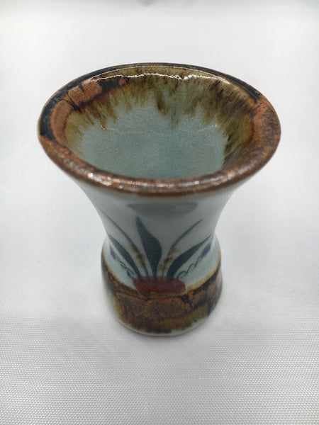 Mini Tequila shot stoneware with brown rim and bottom.   It is natural grey clay color background with birds, butterflies, and leaves in blue, green, black and brown on the outside.