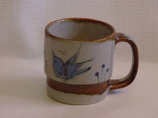 Ken Edwards Mug Cylinder 3.75"x5.25" (T1)  is natural grey clay color with brown rim and handle .  The outside of the mug is decorated with birds , butterflies, and leaves.