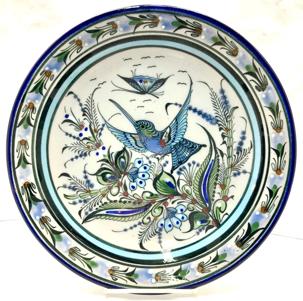 Ken Edwards Colleciton series dinner plate with blue rim. It is natural grey clay color background with birds, butterflies, and leaves in blue, green, black and brown on the outside.  