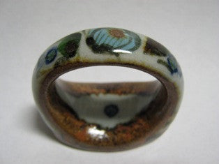 Ken Edwards Napkin Ring (U36) is natural grey clay color with brown blue and green glazes.  it has flowers and butterflies on it.  It hold a  cloth napkin for a somewhat formal dinner.