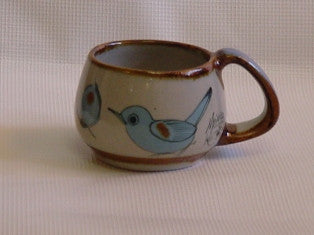 Ken Edwards Mug Rounded 3" tall x 4" wide (T8)  Brown rim.   It is natural grey clay color background with birds, butterflies, and leaves in blue, green, black and brown on the outside.
