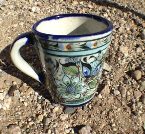 Ken Edwards Collection Series coffee mug in lead free stoneware.  Blue rim and handle .   It is natural grey clay color background with birds, butterflies, and leaves in blue, green, black and brown on the outside.