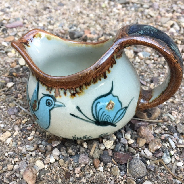 Ken Edwards cream pitcher in brown rim and handle along with blue, black and green butterflies or birds and leaves.