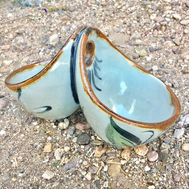 Ken Edwards Stoneware Pottery in natural grey clay color with brown rim and blue, green, and black birds, butterflies and leaves decorated on the exterior on vases, interior on plates , trays and triviets.  this is a double dipper salsa bowl or a hanging double plant holder.